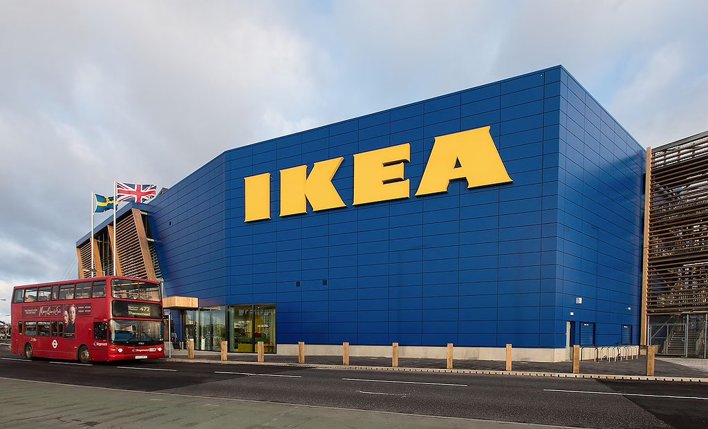 A London double decker bus driving by IKEA's Greenwich store with flags flying. 